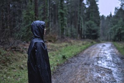 Woman wearing raincoat while standing on footpath at forest