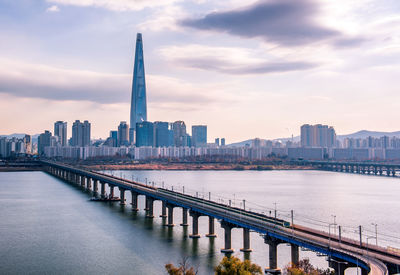 Bridge over river by buildings in city against sky