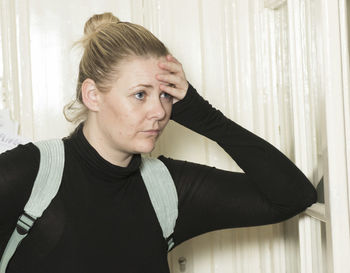 Portrait of young woman looking away while standing against window at home