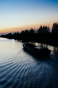 Silhouette boats in river against clear sky at sunset