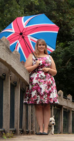 Low angle view of young woman holding umbrella while standing by railing on bridge