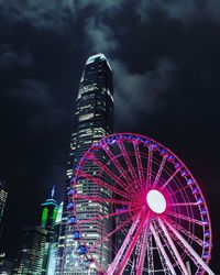 Low angle view of illuminated ferris wheel against buildings at night