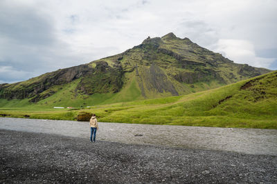 Rear view of woman standing by stream against mountain