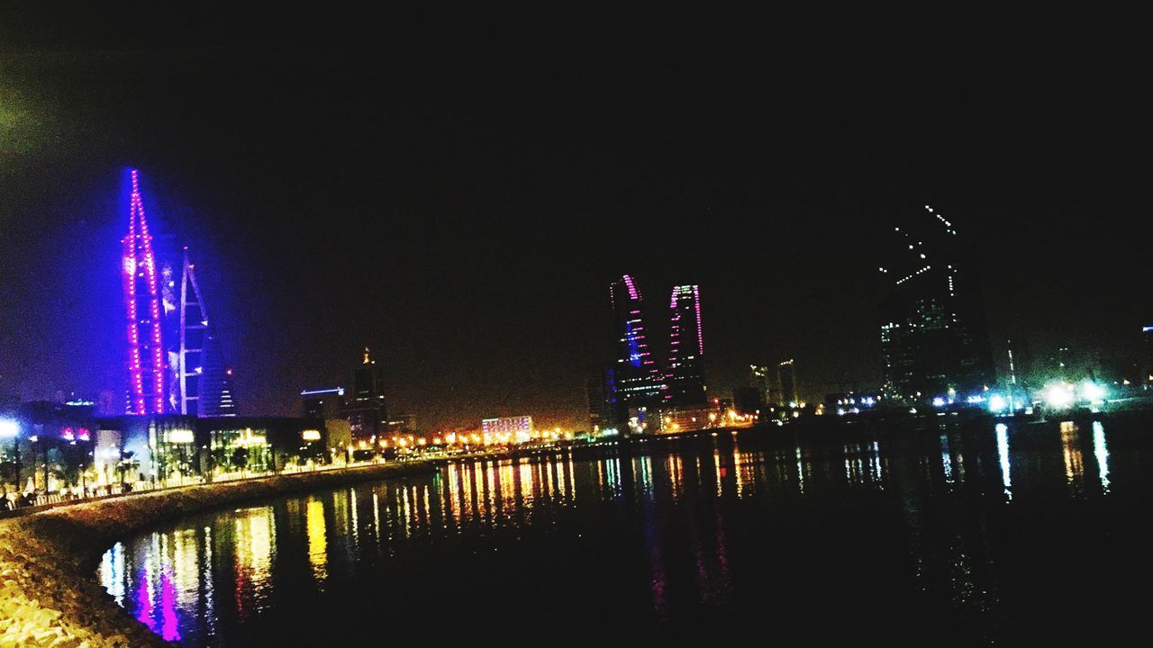 ILLUMINATED MODERN BUILDINGS BY RIVER AGAINST CLEAR SKY AT NIGHT