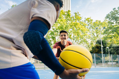 Multiracial friends players running together with ball while playing basketball on sports ground in sunny day