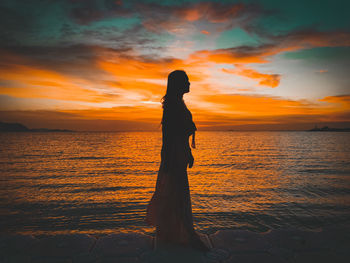 Silhouette woman standing by sea against sky during sunset