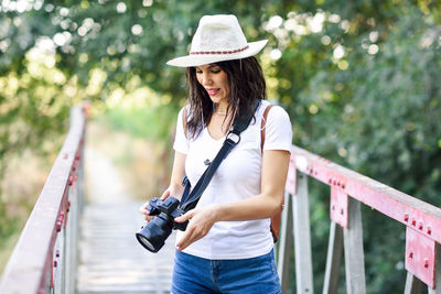 Woman holding camera while standing by railing