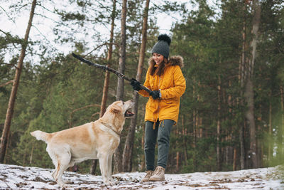 Young woman in yellow jacket trains big kind white dog labrador walking in winter forest