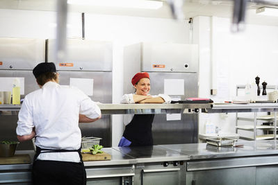 Smiling female chef leaning on counter with student working in cooking school