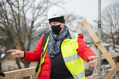 Portrait of thoughtful civil engineer architect wearing hardhat and black face mask at building site