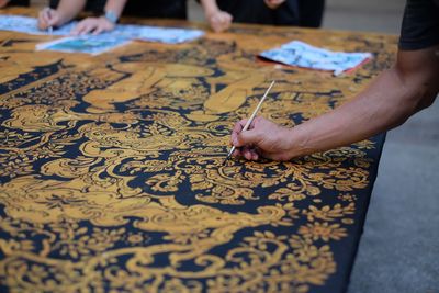 Cropped hand of craftsperson making design on fabric at workshop