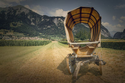 Horse cart on field by mountains against sky