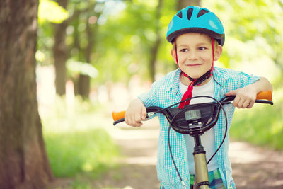 Portrait of smiling boy with bicycle standing against trees