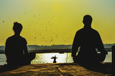 Silhouette men sitting by sea against clear sky during sunset