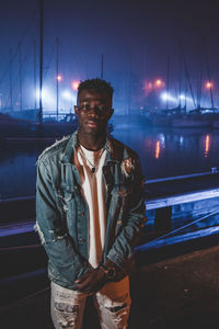 Portrait of young man standing at harbor in night