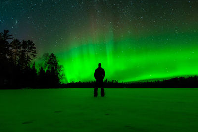 Silhouette of man standing on field against sky at night with northern lights
