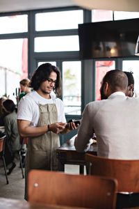 Young owner using credit card reader while standing by male customers at restaurant