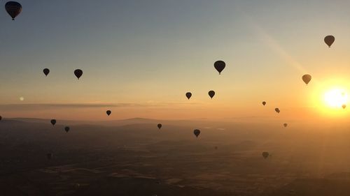 Silhouette hot air balloons flying over landscape during sunrise