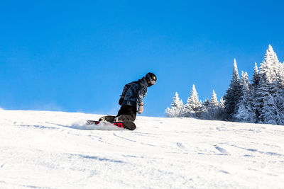 Man snowboarding on snowy landscape against clear blue sky