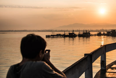 Rear view of man photographing by sea gainst sky during sunset