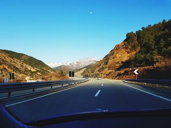 Road seen through car windshield against clear blue sky