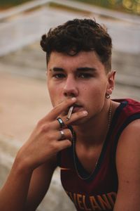 Portrait of young man smoking cigarette sitting outdoors