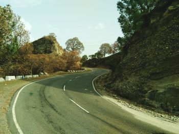 Empty road amidst trees against sky