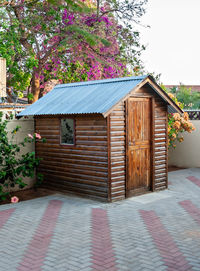 Wooden house amidst plants and trees in yard against sky