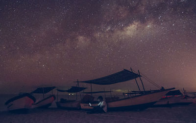 Man sitting by boat at beach against sky at night