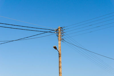 Low angle view of electricity pylon against clear blue sky