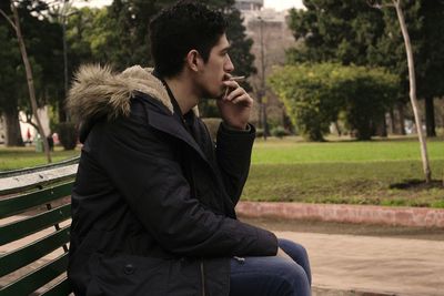 Side view of man smoking marijuana while sitting on bench at park