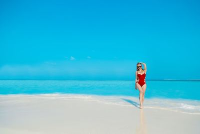 Woman walking at beach against clear blue sky