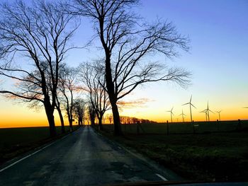 Road amidst bare trees against sky during sunset