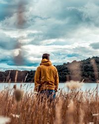 Rear view of young man standing in agricultural field by sea against sky