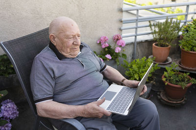 Senior man with laptop sitting on balcony