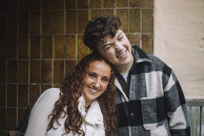 Portrait of smiling girl leaning on male friend against wall