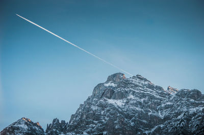 Low angle view of snow covered mountains against blue sky