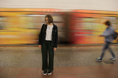 Blurred motion of train at railroad station and static girl