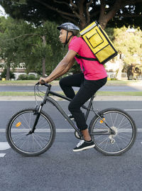 Male delivery person with yellow backpack riding bicycle on street