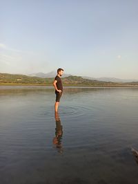 Side view of man standing in water against sky