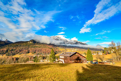 Scenic view of field by houses against sky