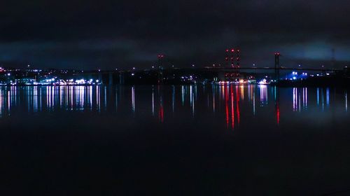 Illuminated city by river against sky at night