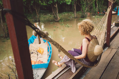 Side view of woman sitting on hammock over river