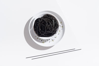 From above of ceramic bowl with delicious spaghetti with black squid ink with chopsticks on white background