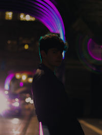 Portrait of young man standing against illuminated lights at night