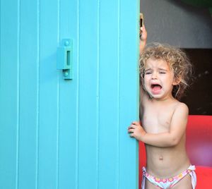 Cute crying girl standing by blue door