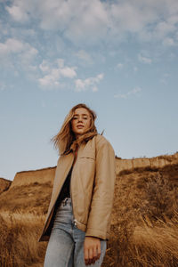 Portrait of young woman standing by plants against sky