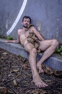 Portrait of naked man siting by wall outdoors