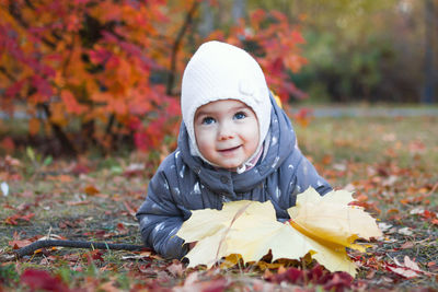 Cute little girl is lying on a grass with yellow leaves on a walk in autumn park.
