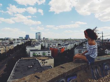 Woman sitting in city against sky